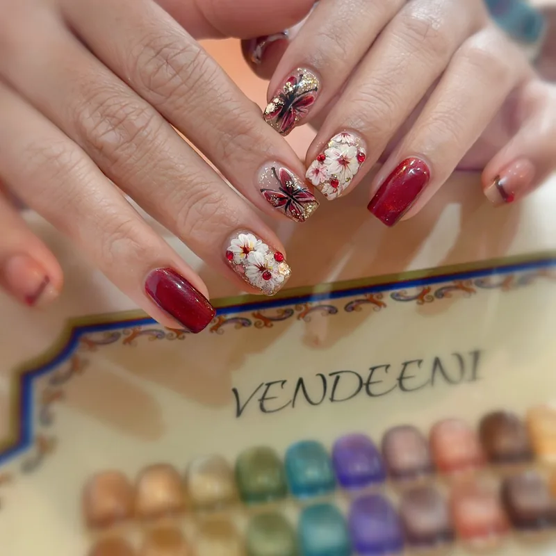 Deep red gel nails with white 3D blossoms and a butterfly accent